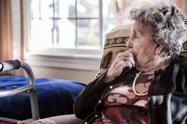 Older woman sat in a comfortable armchair with a contemplative look.