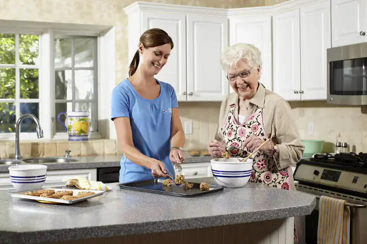 Older lady being supported by a carers in the kitchen. They are baking cookies together.