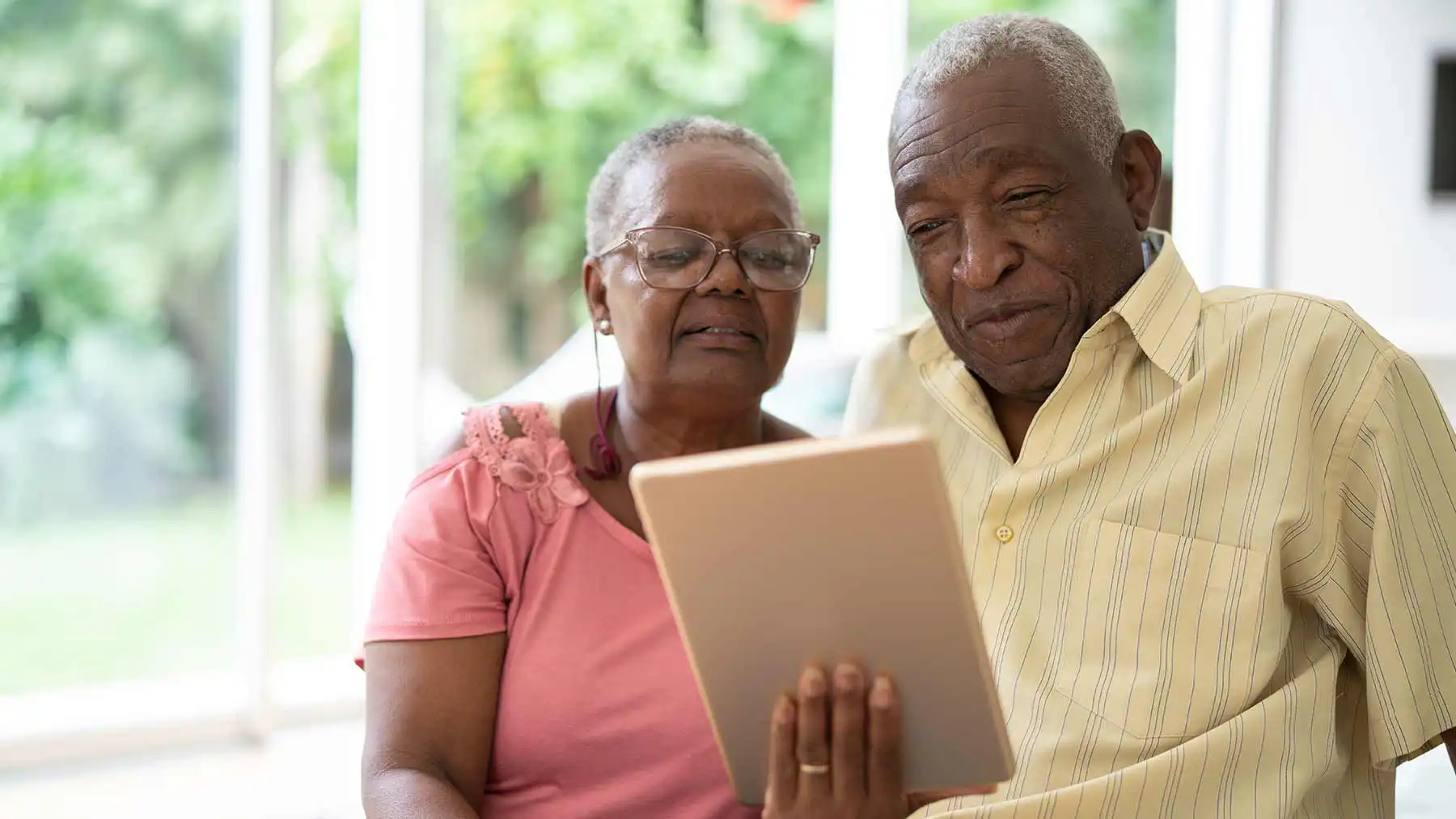 Elderly couple sat next to each other looking at a handheld tablet.