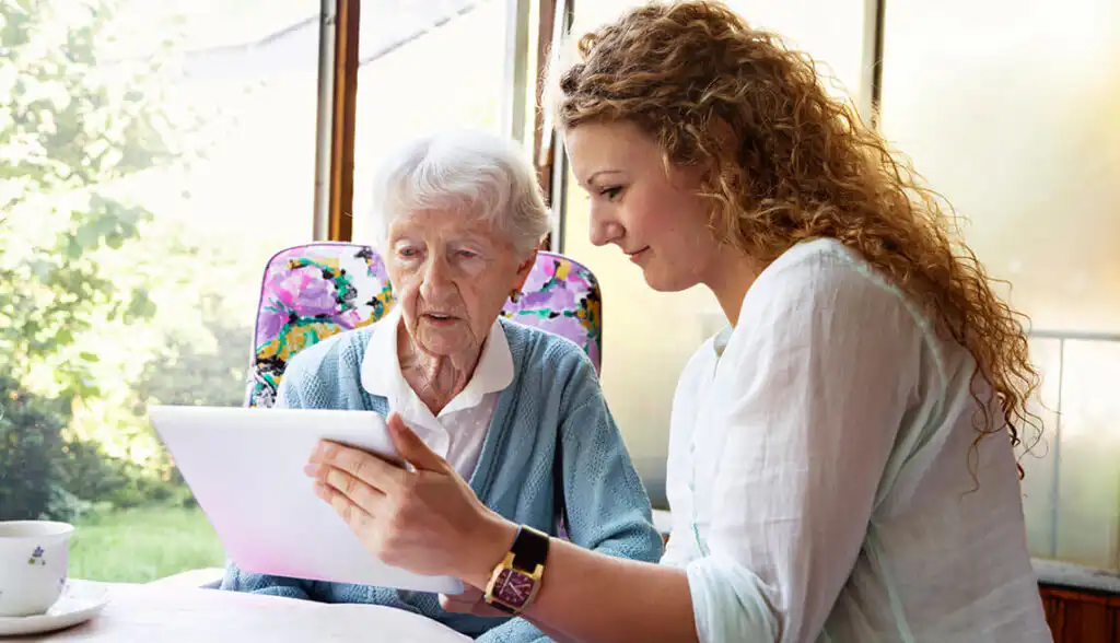 Older woman sitting next to a younger woman and being shown something on a handheld tablet.