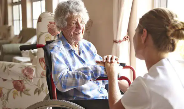 Older woman in a wheelchair smiling at her carer who is knelt down in front of her.