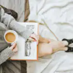 Arial view of someone sat cross legged with a book on their lap drinking a cup of tea.
