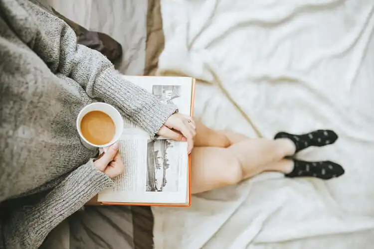 Arial view of someone sat cross legged with a book on their lap drinking a cup of tea.