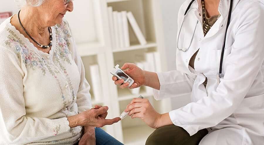 A doctor in a white coat checks an elderly woman's blood sugar with a glucometer. The scene conveys care and medical attention in a clinical setting.