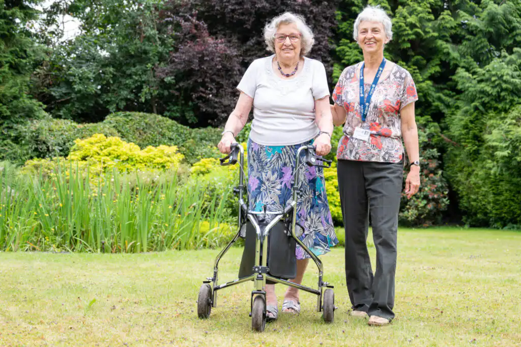 Elderly client being assisted by their live-in carer to take a walk in the garden.