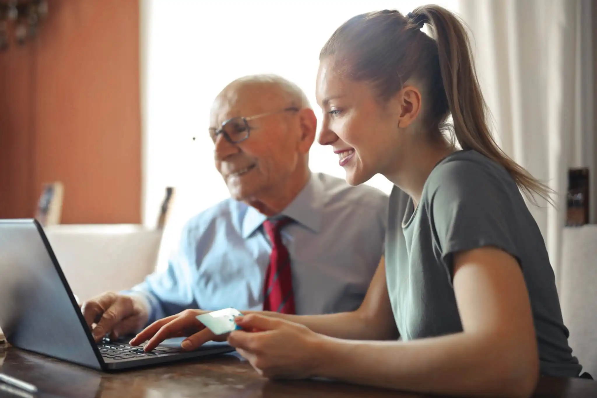 Older man being supported to use a laptop by his carer