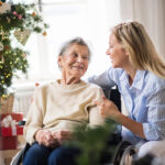 An elderly women and a relative together with a Christmas tree in the background.