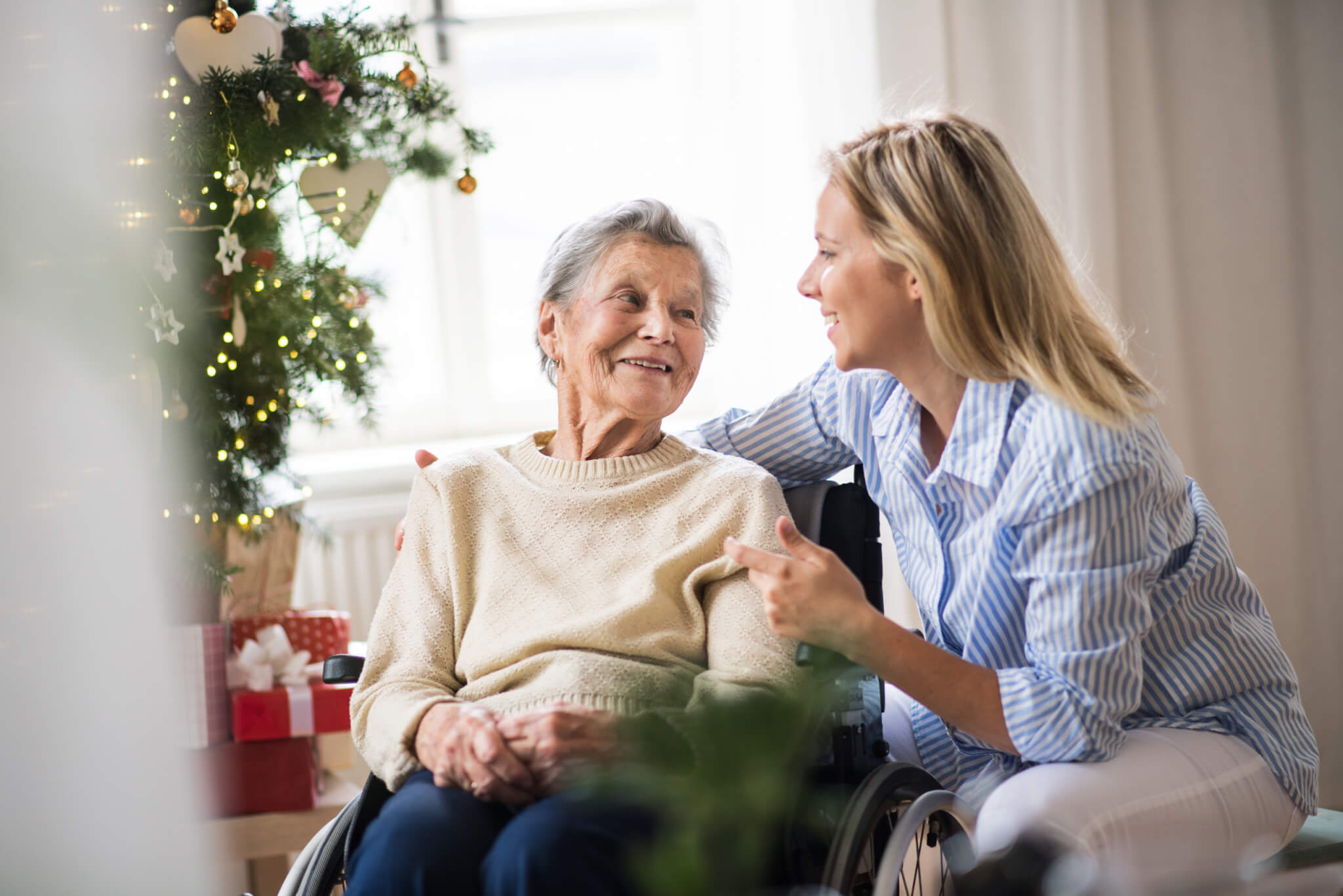An elderly women and a relative together with a Christmas tree in the background.