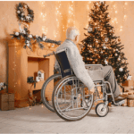 An elderly person in a wheelchair looks at a decorated Christmas tree and a mantel adorned with lights and wreaths.