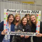 Five smiling people hold a colourful "Proud of Bucks 2024" frame. The person in front holds an award.