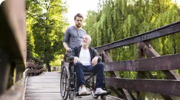 Man in wheelchair being assisted on an outing by his live-in carer