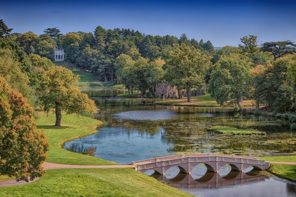 View across Serpentine Lake in Cobham Surrey UK, with trees lining the banks and a bridge across the water.