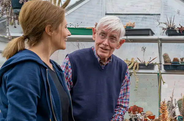 Man with live-in carer talking in potting shed.