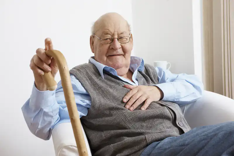 Elderly gentleman sitting in chair with walking stick, smiling at the camera