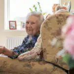 Elderly lady sitting in armchair in the comfort of her own home, smiling at the camera