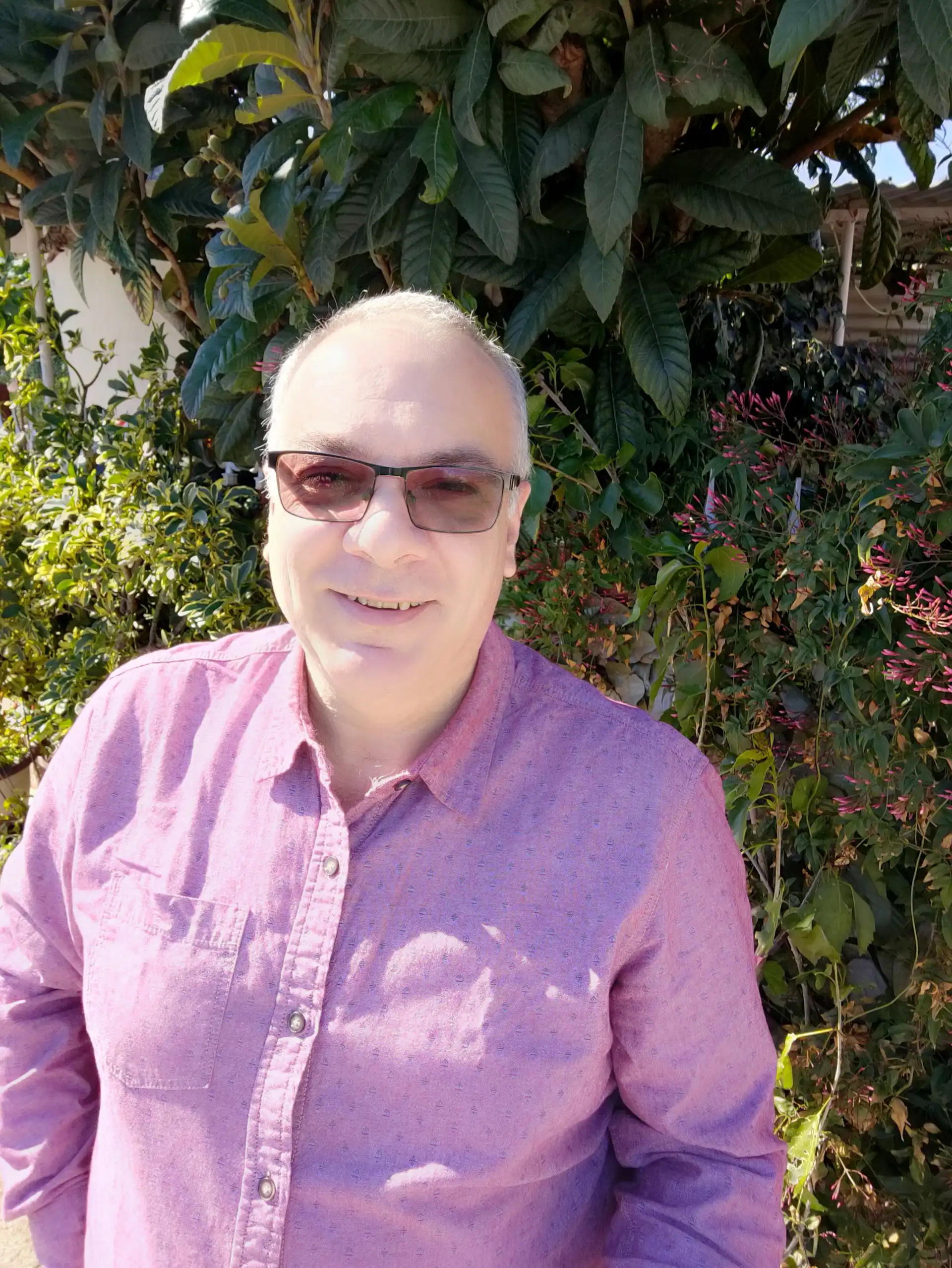 Professional male carer photographed outside with tress in the background. He is smiling warmly at the camera.