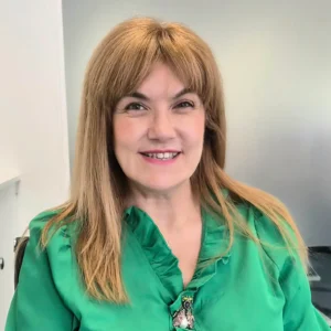 Woman in a green shirt smiling warmly at the camera whilst seated in the Ashridge Home Care office.