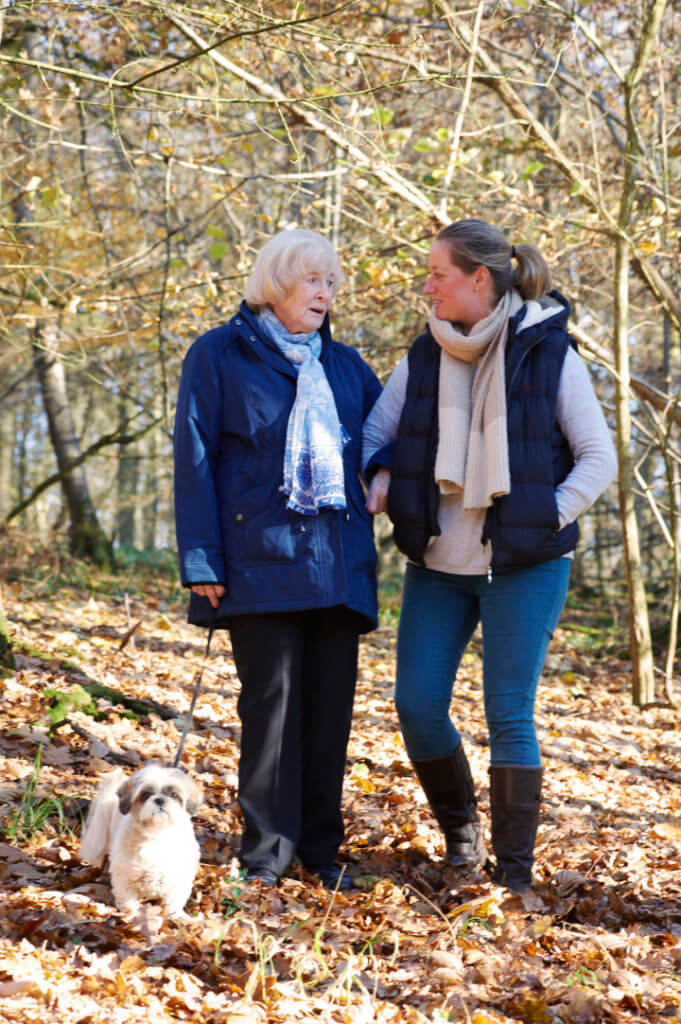 MND care-elderly lady walking the dog with carer in the woods